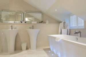 Contemporary bathroom at Greenwoods Hotel Attic Suite with sleek pedestal sinks, large mirrors, and freestanding bath under a sloped ceiling.