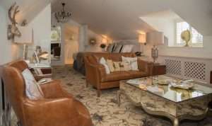 Spacious attic suite at Greenwoods Hotel featuring leather seating, mirrored coffee table, and elegant sloped ceilings for a luxurious stay experience.