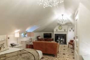 Luxurious Attic Suite at Greenwoods Hotel featuring a fireplace, plush leather chairs, crystal chandeliers, and warm ambient lighting.