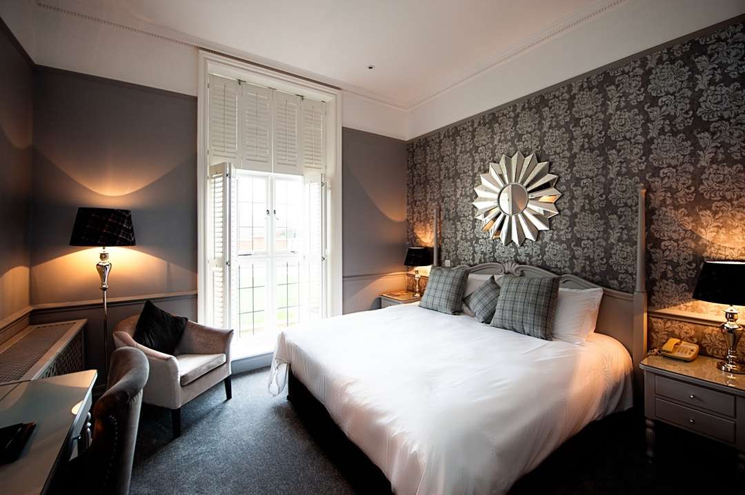 Elegant hotel bedroom with grey tones and decorative mirror, perfect for promoting housekeeping job roles at Greenwoods Hotel.