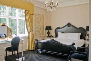 Sophisticated hotel bedroom at Greenwoods with bold black headboard, gold-accented curtains, and vanity dressing table.