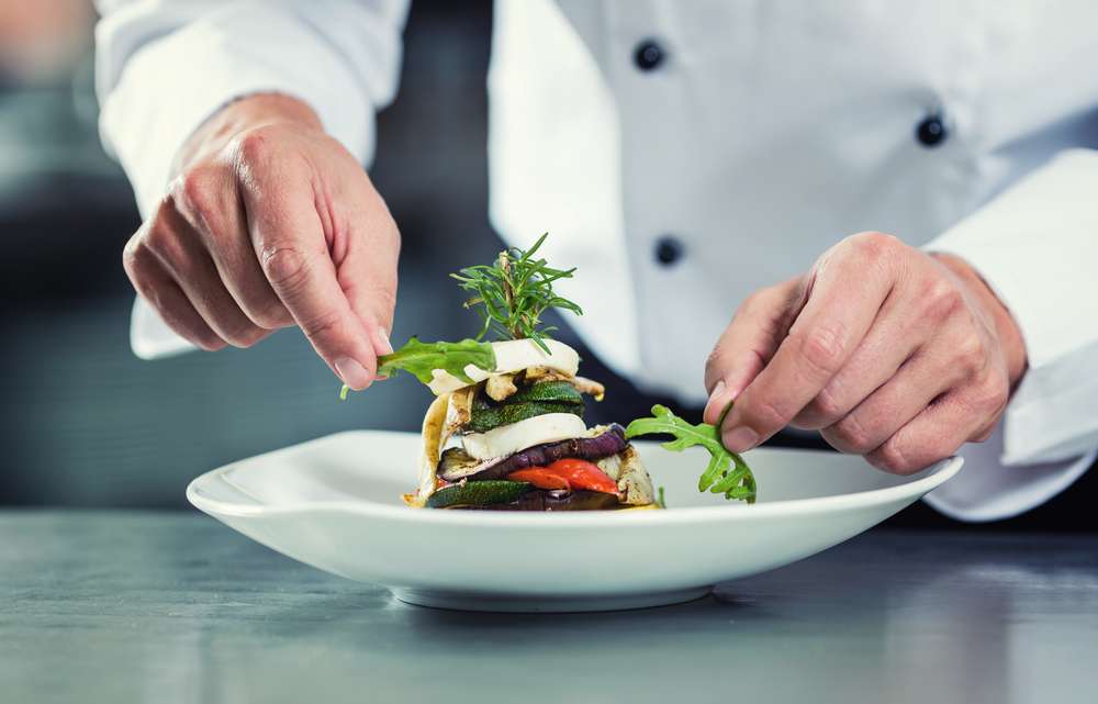 Chef de Partie applying garnish to a stacked vegetable dish at Greenwoods Hotel, showcasing culinary finesse.