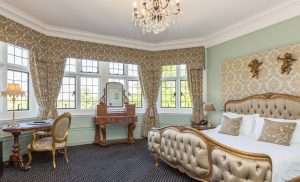 Classic style bedroom at Greenwoods Hotel with tufted gold headboard, bay windows, and luxurious vintage furniture.