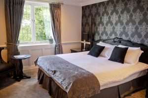 Moody and stylish Manor Classic bedroom at Greenwoods Hotel featuring black carved headboard and damask wallpaper accent wall.
