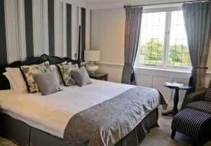 Bright and modern Manor Room at Greenwoods Hotel showcasing black and white striped wall, floral cushions, and green countryside views.