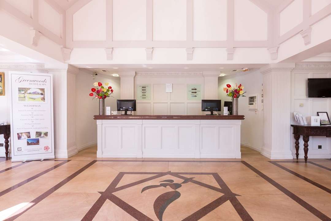 Reception area at Greenwoods Hotel with computers and floral arrangements, ideal for representing a Night Porter role.