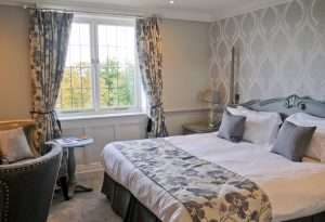 Manor Classic bedroom at Greenwoods Hotel with silver tones, matching curtains, floral feature wall and soft grey upholstery.