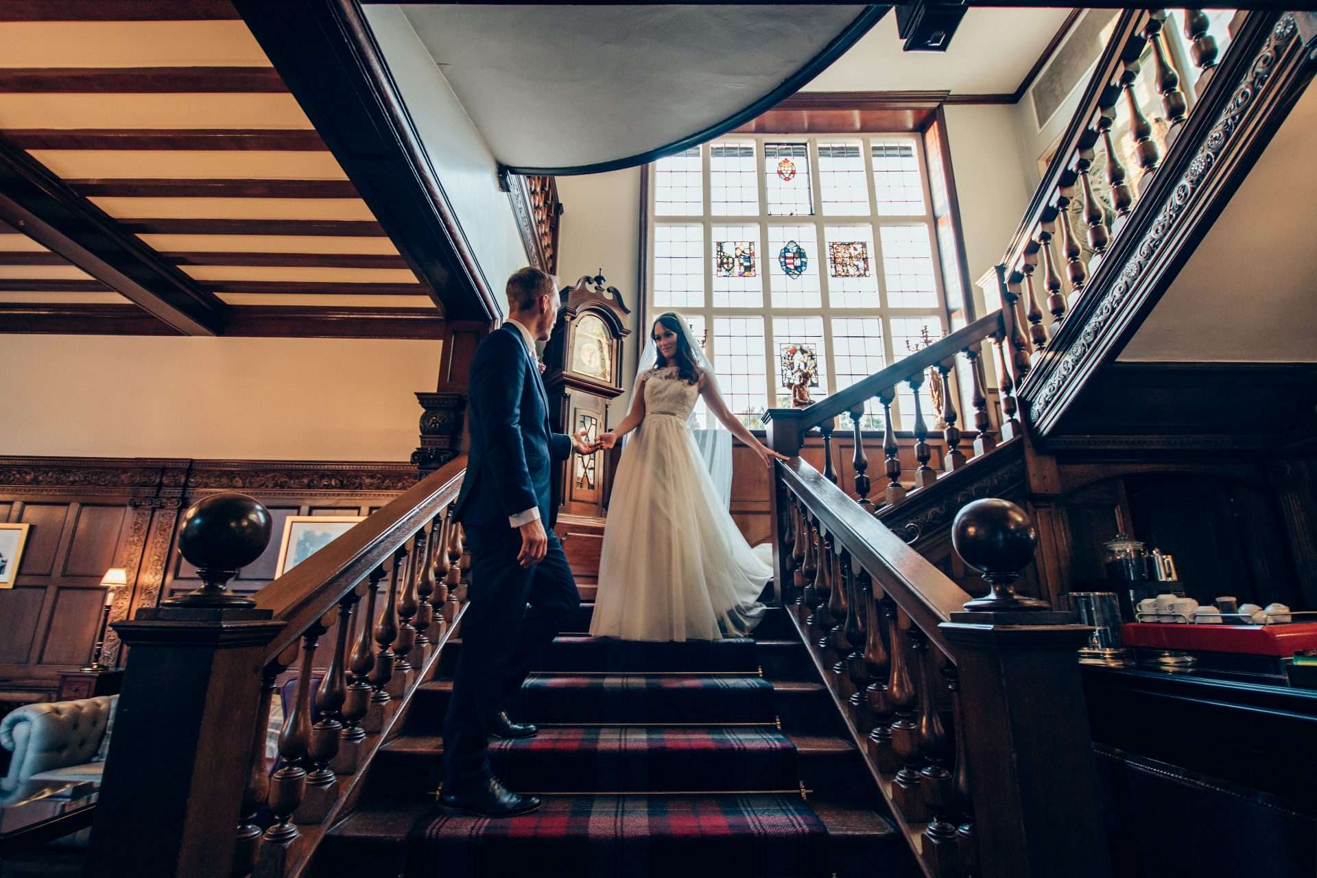 Bride and groom on the elegant wooden staircase inside Greenwoods Hotel, with stained glass window backdrop