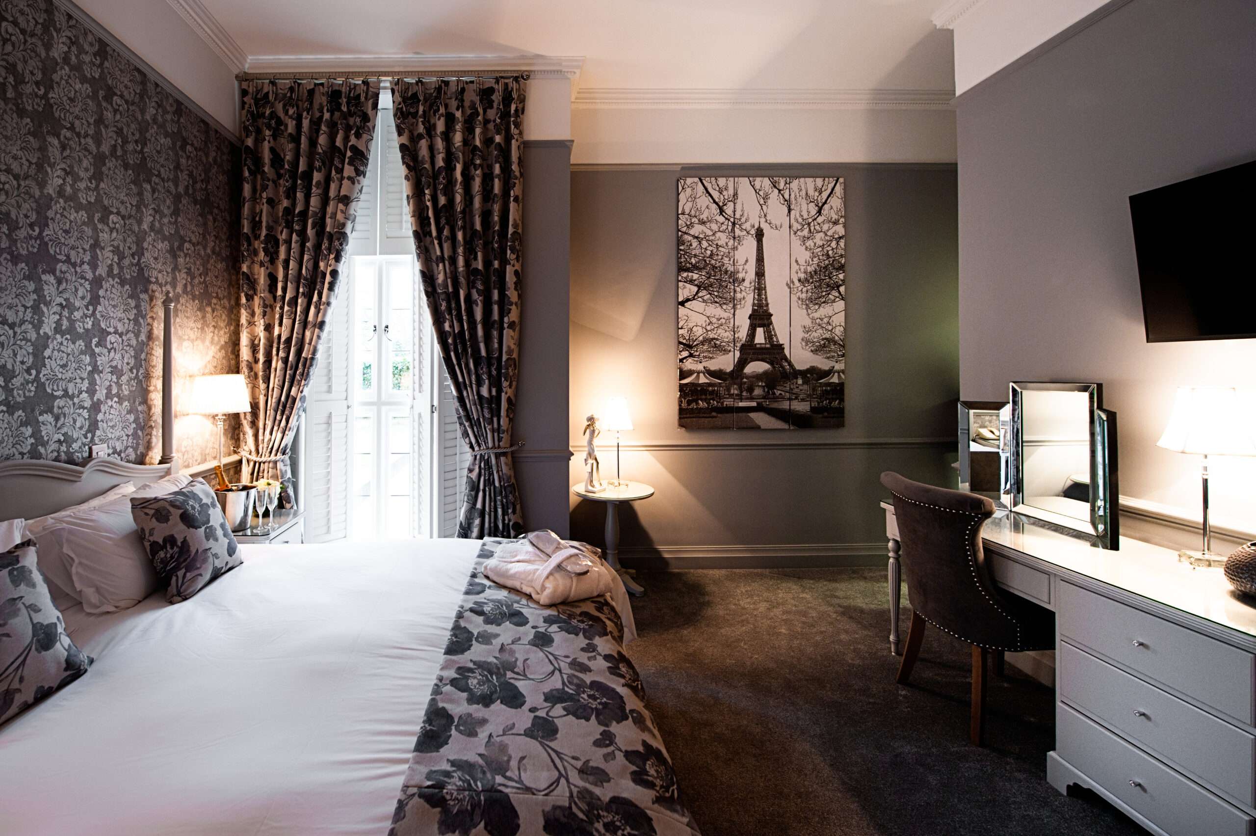Hotel room at Greenwoods with Paris-themed art, dark floral wallpaper, and plush décor
