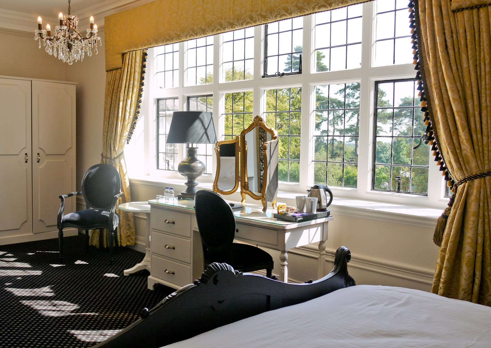 Room at Greenwoods Hotel featuring large gold mirror, black chair, and beautiful window views
