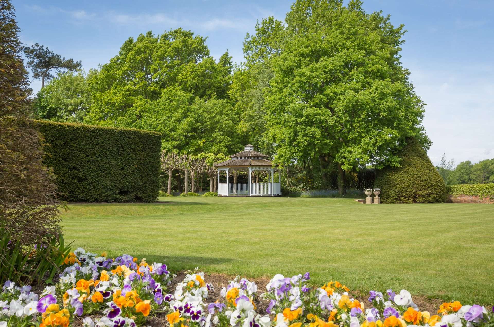 View of the wedding gazebo at Greenwoods Hotel surrounded by trees and lawn with flower beds