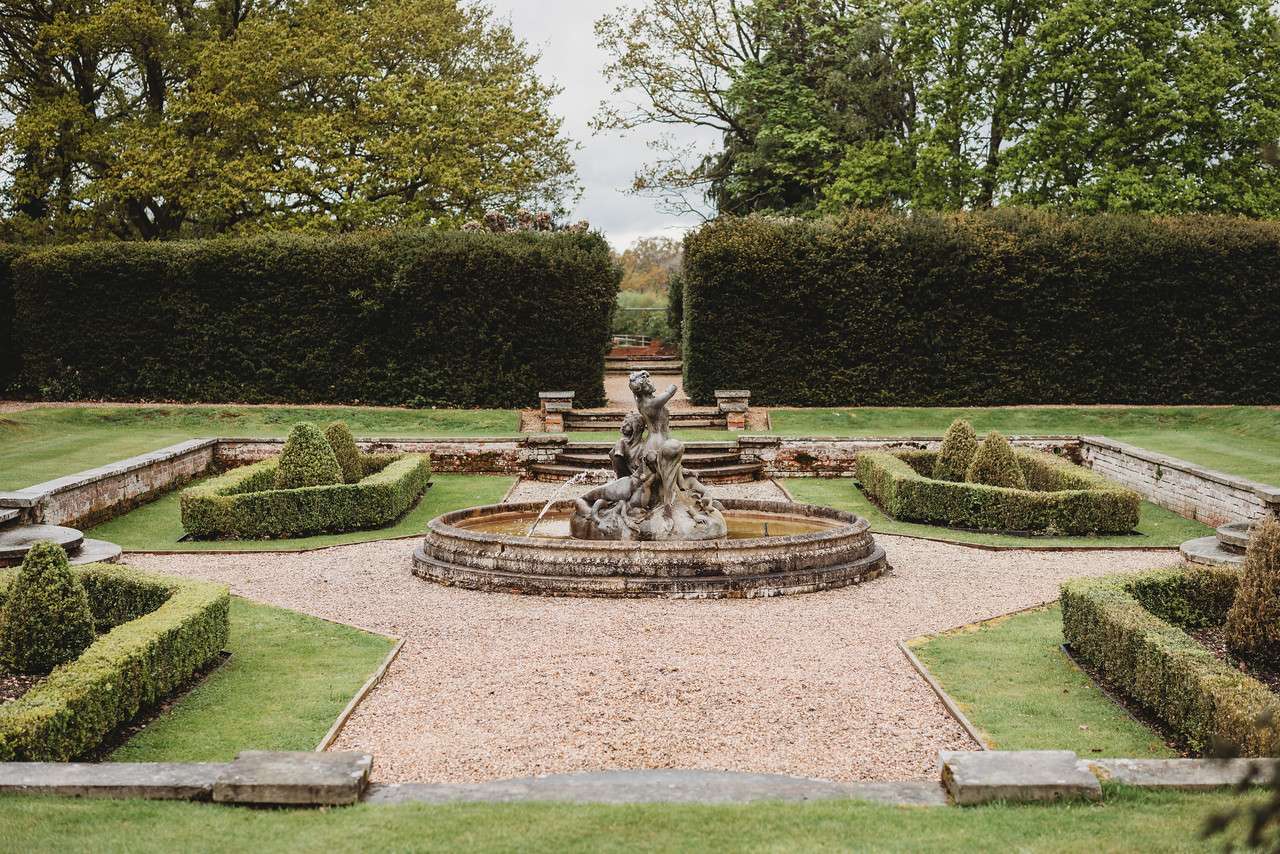 Stone sculpture fountain surrounded by manicured hedges at Greenwoods Hotel