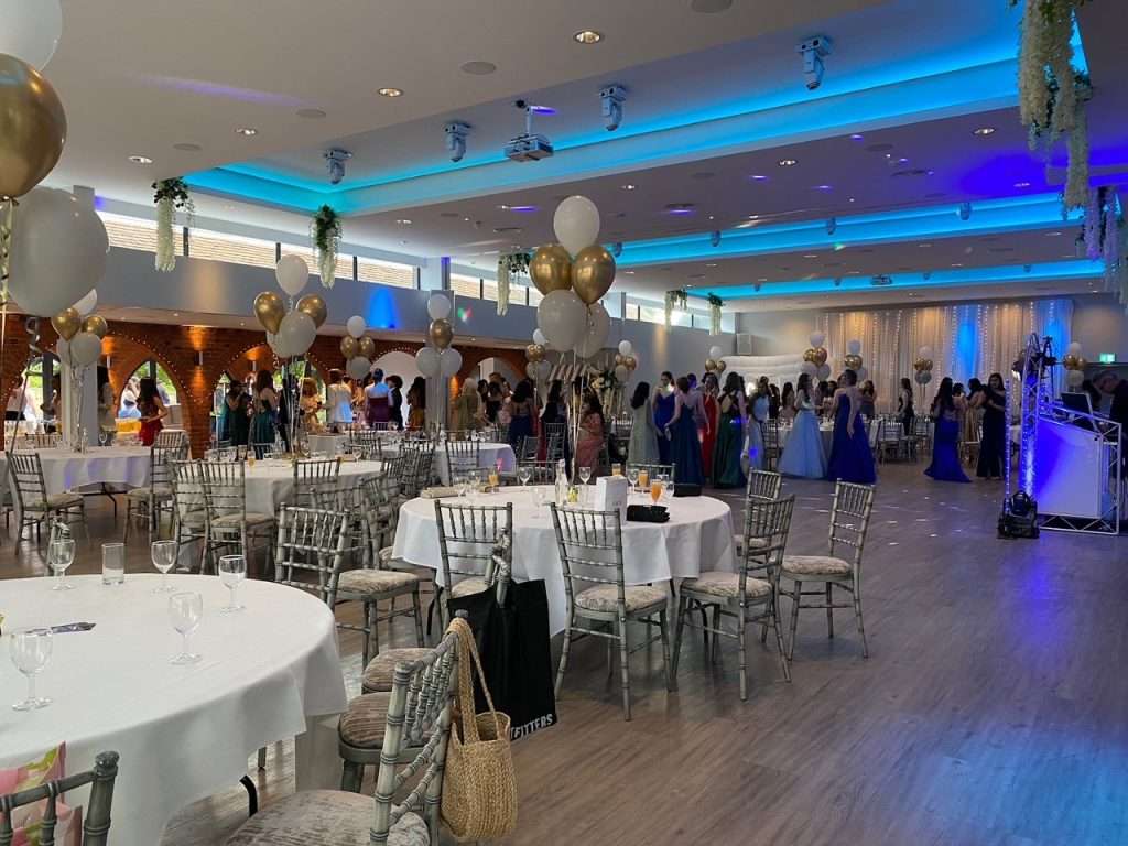 School prom guests enjoying the dance floor surrounded by elegant table settings and balloon décor.