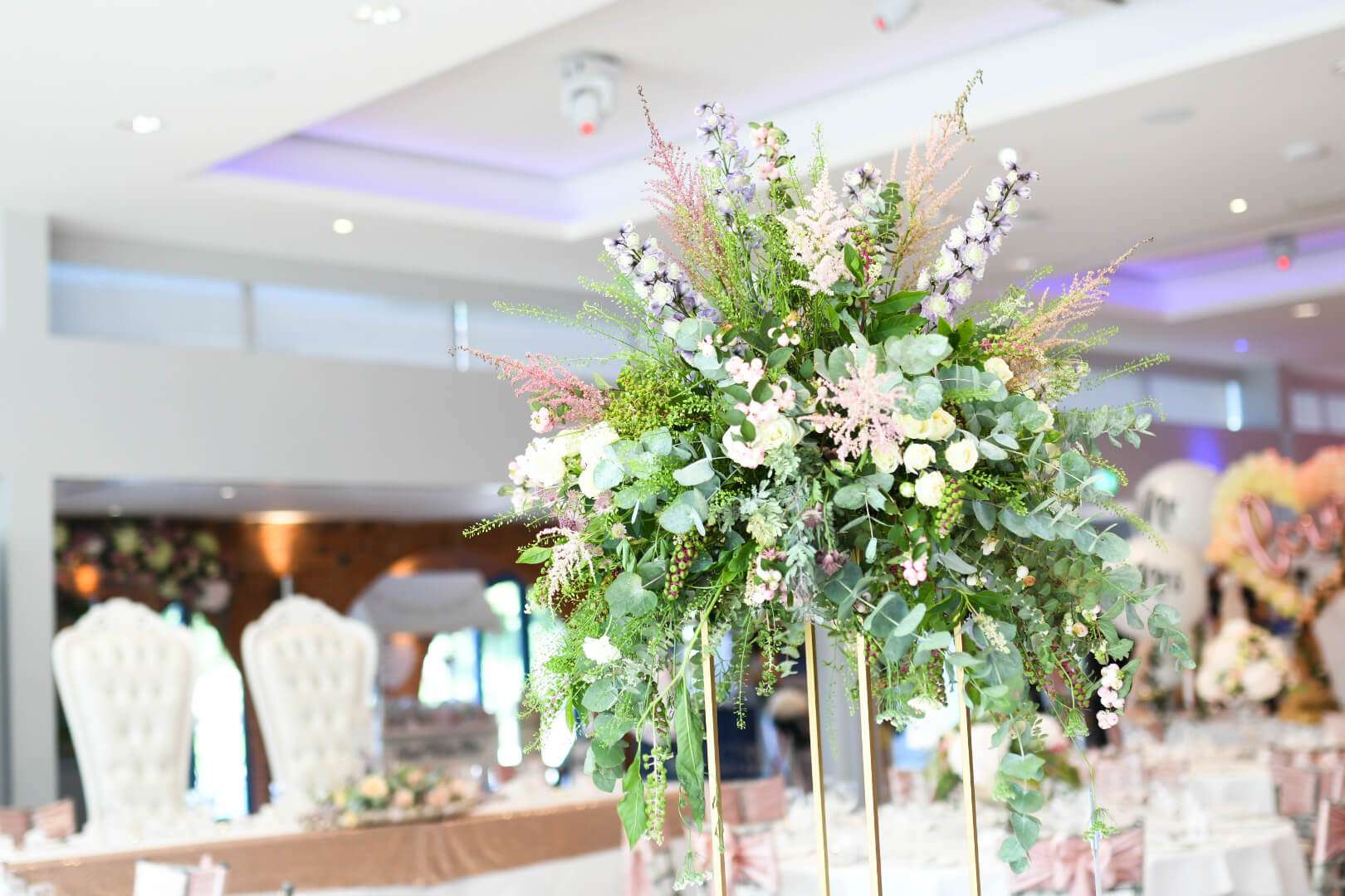 Close-up of tall floral centrepiece at Greenwoods Hotel wedding reception with elegant table décor in background