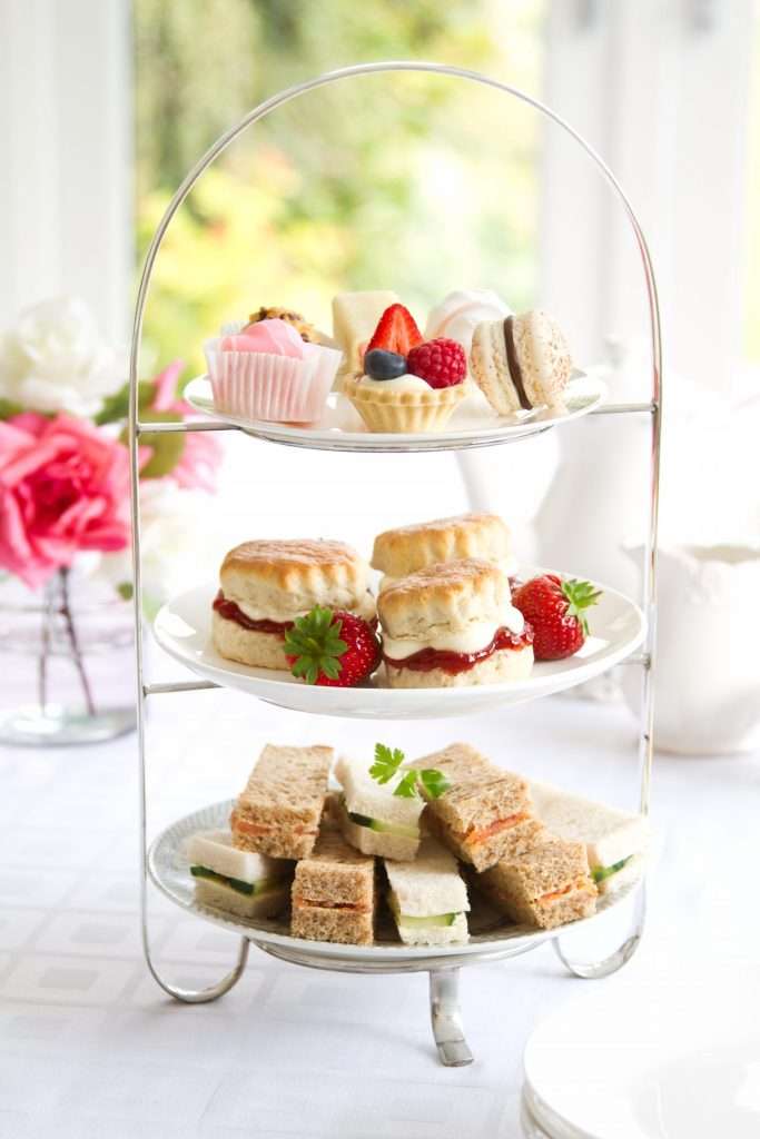 Close-up of a traditional three-tiered afternoon tea stand featuring sandwiches, scones with jam and cream, and pastries. Baby Shower / Bridal Shower set up for afternoon tea