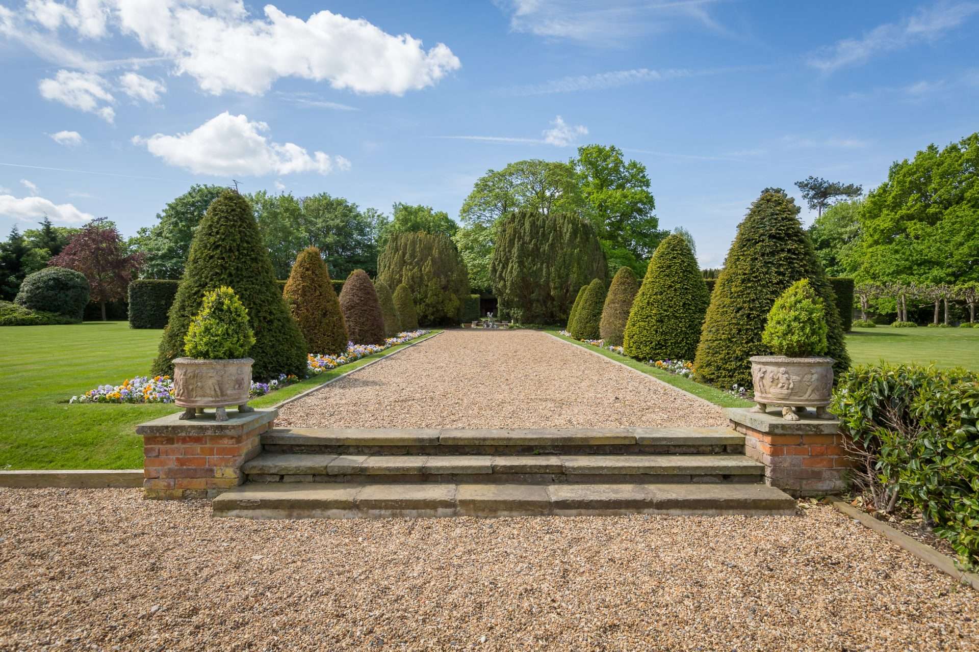 Gravel walkway lined with shaped topiary and flower beds in the grounds of Greenwoods Hotel