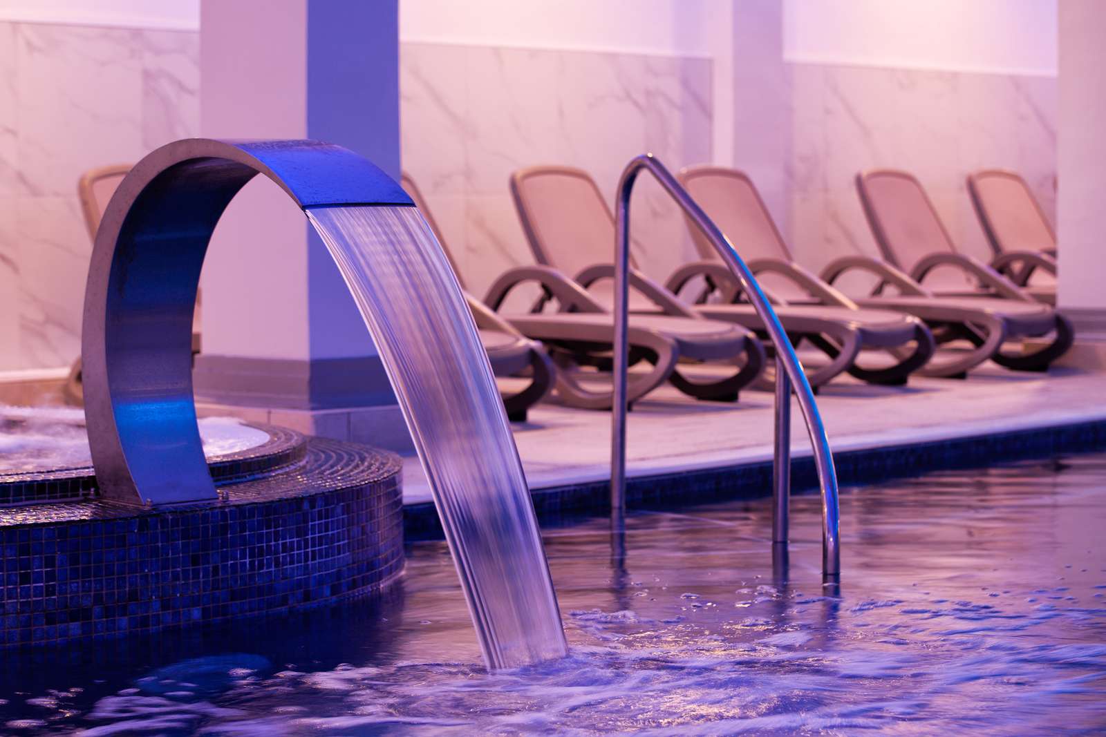 Curved water fountain flowing into spa pool with loungers in the background
