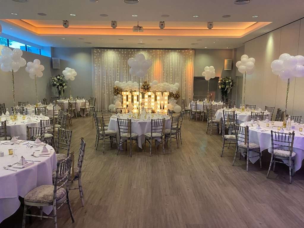 School prom setup with white balloon centrepieces and PROM letters framed by a balloon arch.