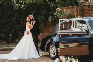 Bride and groom standing beside a classic wedding car in the grounds of Greenwoods Hotel, showcasing the elegance of this dry hire wedding venue in Essex.