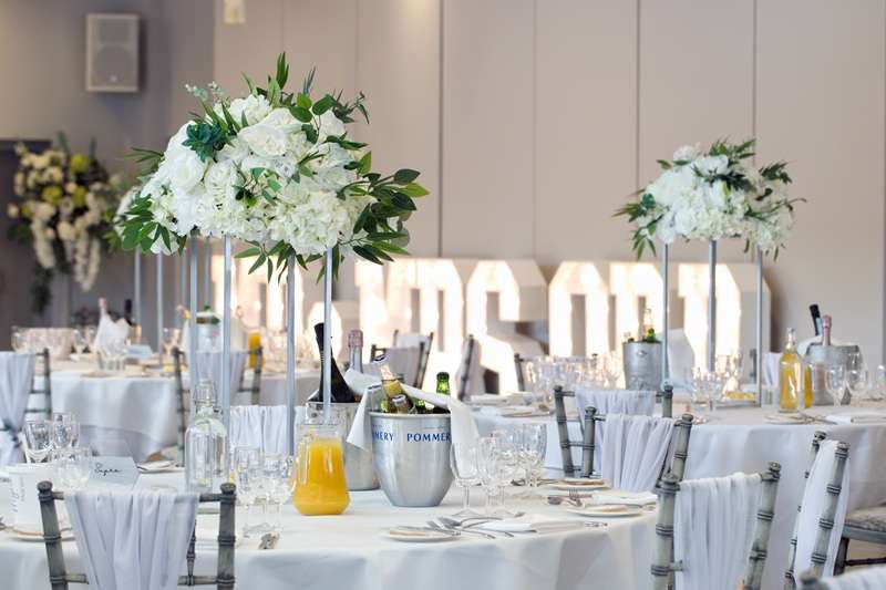 Sophisticated wedding reception at Greenwoods Hotel & Spa in Essex with white floral centrepieces, champagne buckets, and glowing MR & MRS lights.