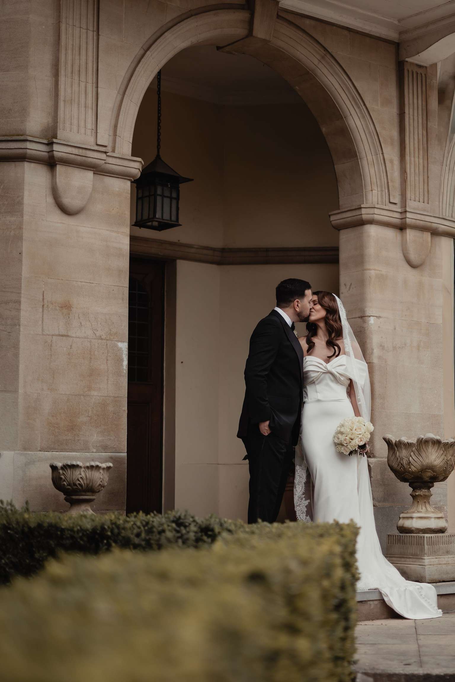 Bride and groom kissing beneath the manor house archway at Greenwoods Hotel and Spa wedding venue.