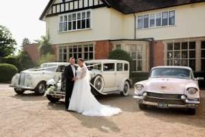 Bride and groom outside Greenwoods Hotel and Spa with classic wedding cars in front of the manor house.