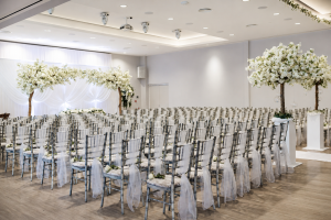Indoor wedding ceremony setup in the Garden Suite at Greenwoods Hotel and Spa, with floral trees, dressed chairs and elegant white decor.
