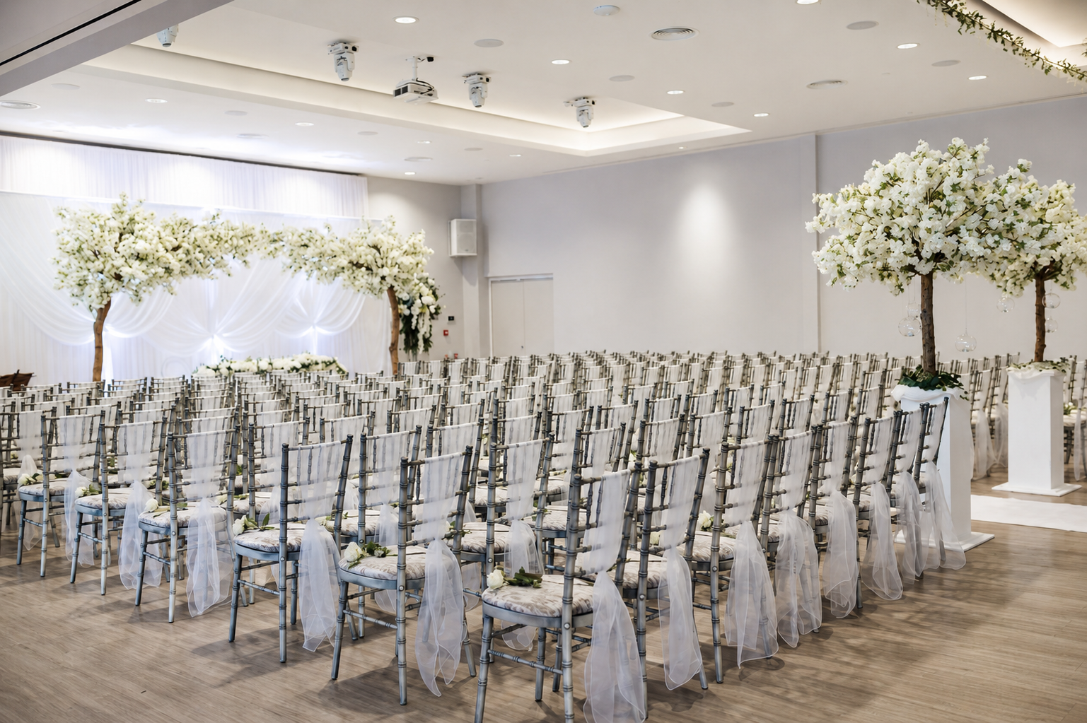 Indoor wedding ceremony setup in the Garden Suite at Greenwoods Hotel and Spa, with floral trees, dressed chairs and elegant white decor.