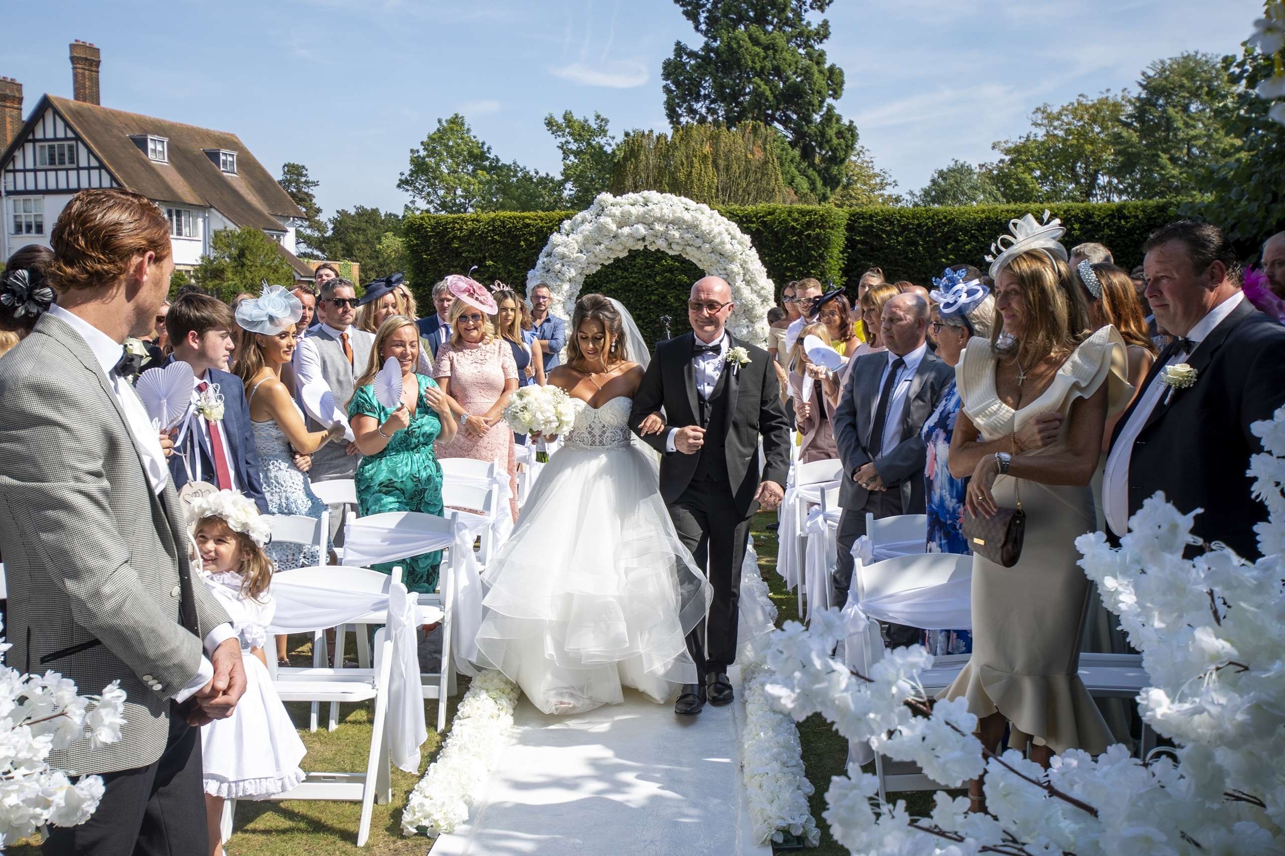 Bride walking down the outdoor garden ceremony aisle at Greenwoods Hotel and Spa, a romantic wedding venue in Essex.