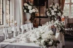 Wedding table decor with white flowers, glassware and dressed chairs inside the manor house at Greenwoods Hotel and Spa.