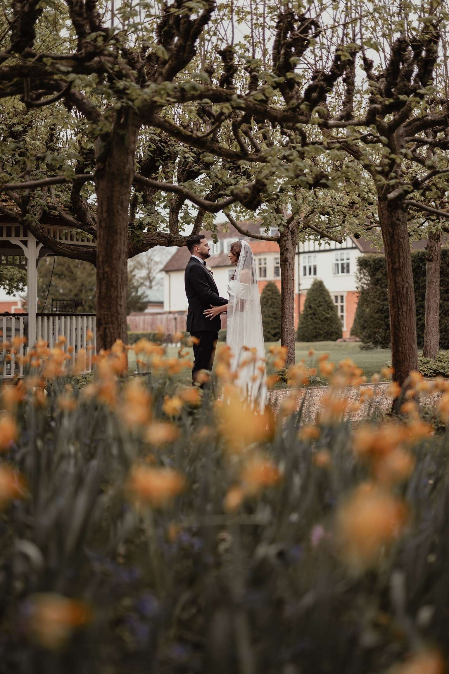 Bride and groom portrait in the gardens at Greenwoods Hotel and Spa, surrounded by trees and seasonal flowers.