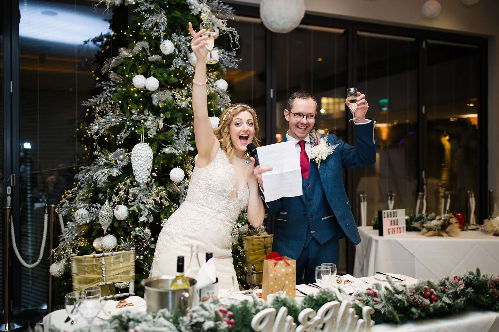 Bride and groom raising champagne during a festive wedding toast beside a Christmas tree at Greenwoods Hotel & Spa in Essex.