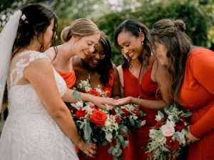 Bride and bridesmaids in red dresses admiring the wedding ring during a Greenwoods Hotel and Spa wedding.