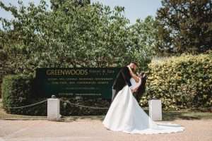 Bride and groom sharing a romantic dip beside the Greenwoods Hotel and Spa sign on their wedding day.