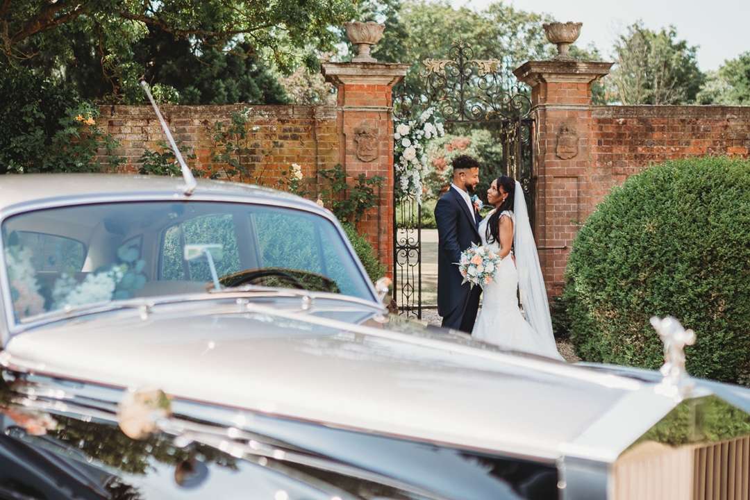 Wedding couple beside a vintage car and garden gate at Greenwoods Hotel & Spa in Essex.