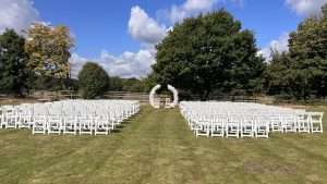 Outdoor dry hire wedding ceremony setup with white chairs and floral arch on the lawns at Greenwoods Hotel and Spa.