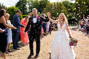 Bride and groom walking through colourful confetti in the gardens at Greenwoods Hotel and Spa wedding venue in Essex.