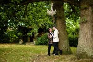 Wedding couple standing together beneath mature trees in the gardens at Greenwoods Hotel and Spa. LGBTQ+ Weddings.