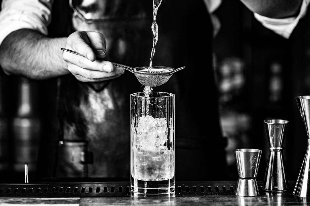 Black and white close up of a bartender preparing a cocktail for a wedding drinks reception.